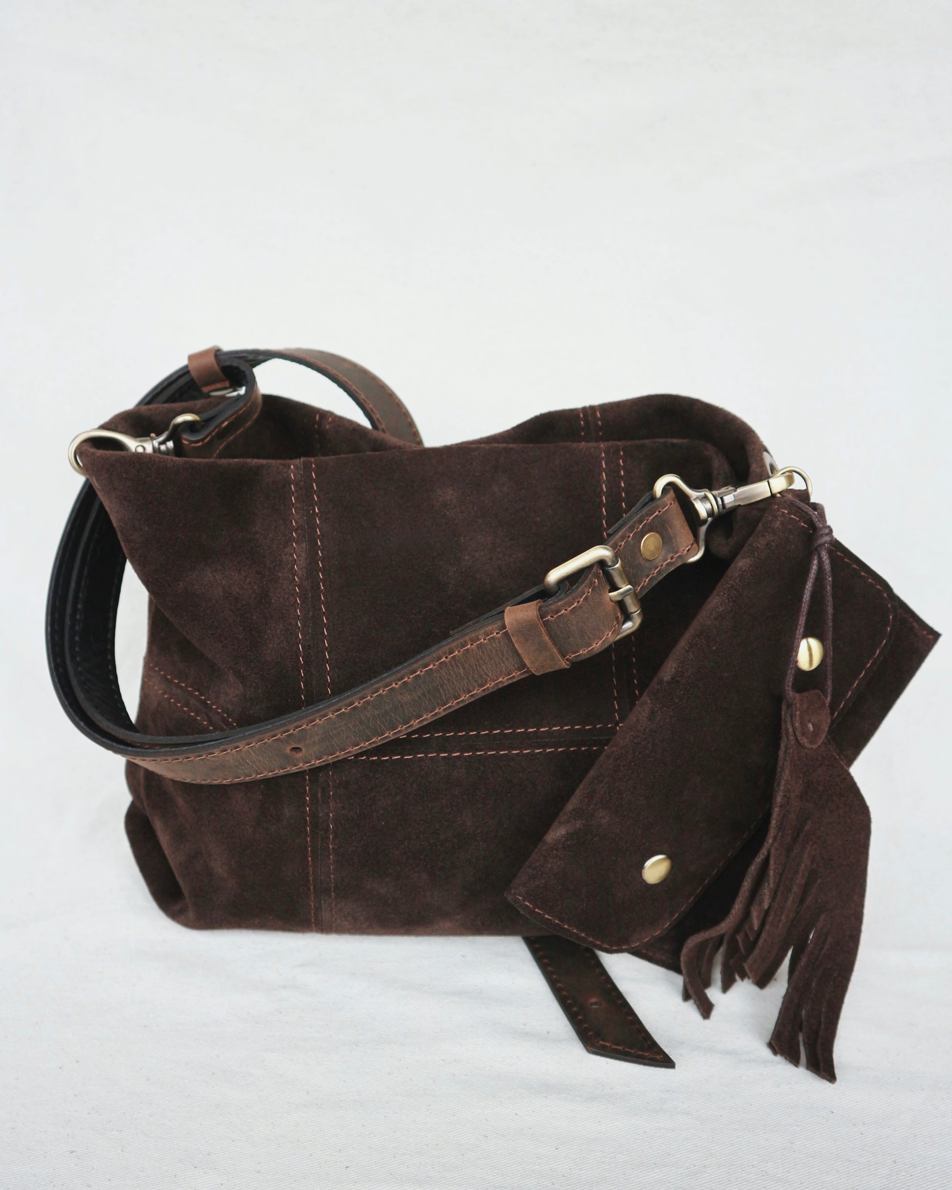 Brown leather handbag with a strap and tassel on a light gray background