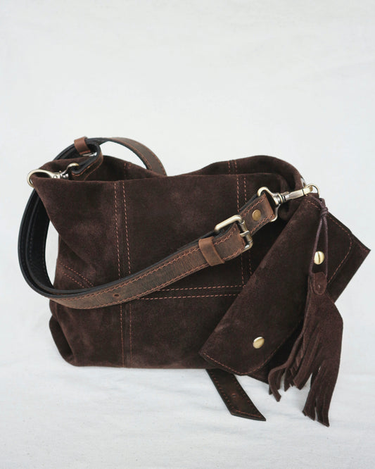 Brown leather handbag with a strap and tassel on a light gray background