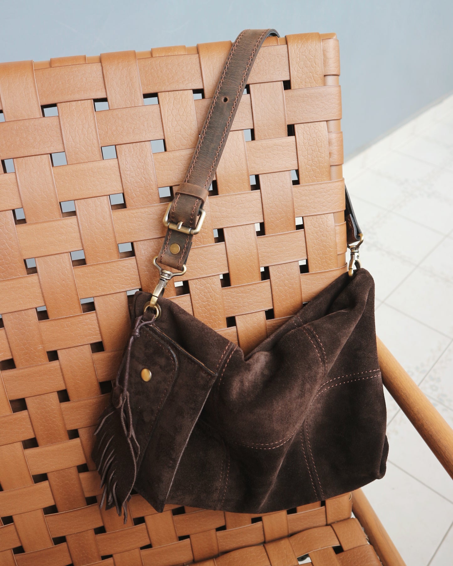 Brown leather handbag hanging on a woven chair with a light blue wall in the background