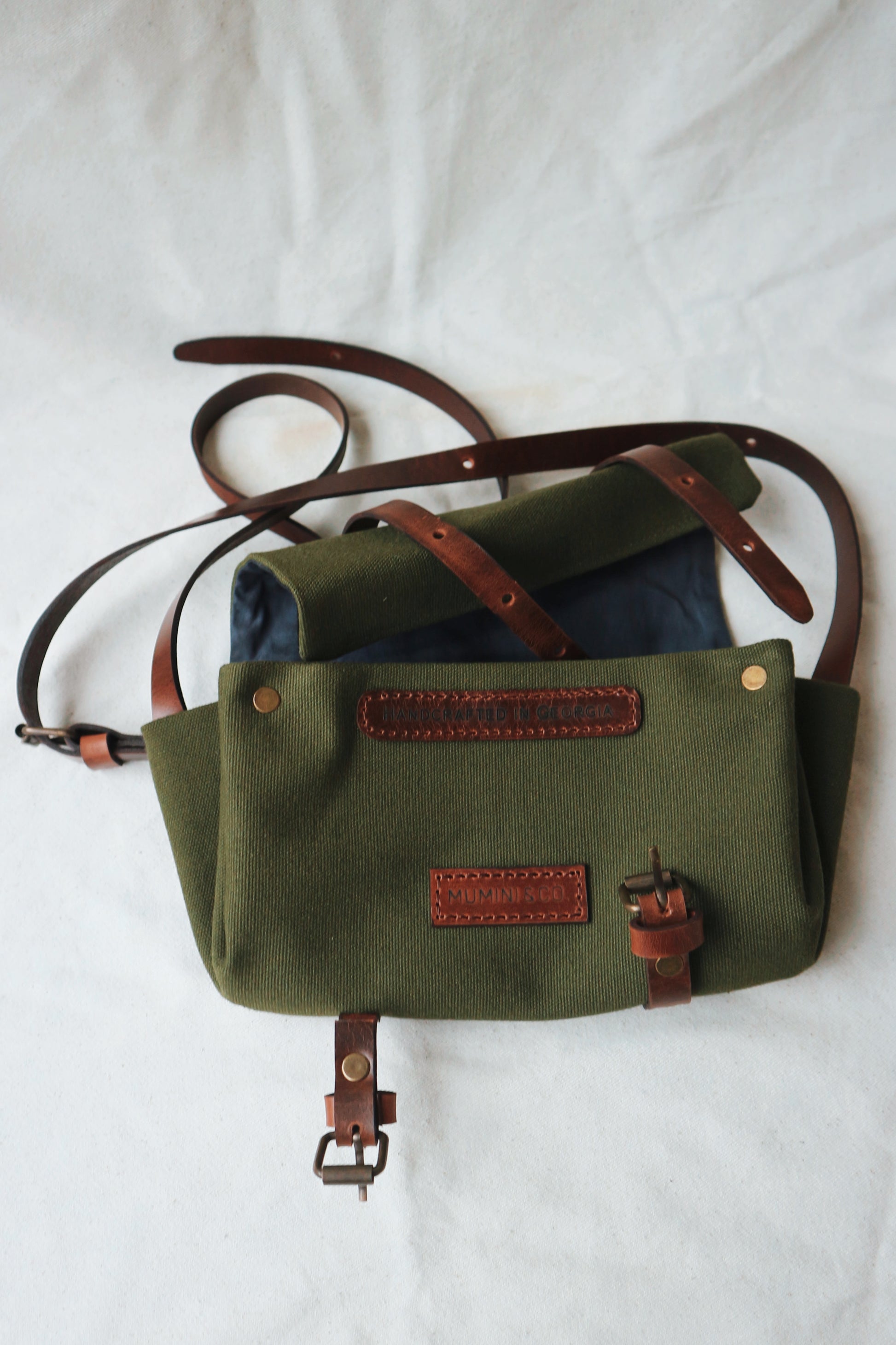 Green canvas bag with brown leather straps on a white background