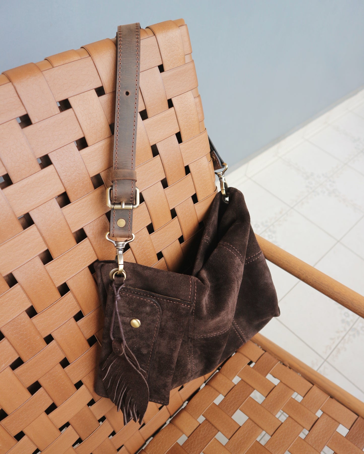 Brown woven handbag with a matching strap on a light blue background