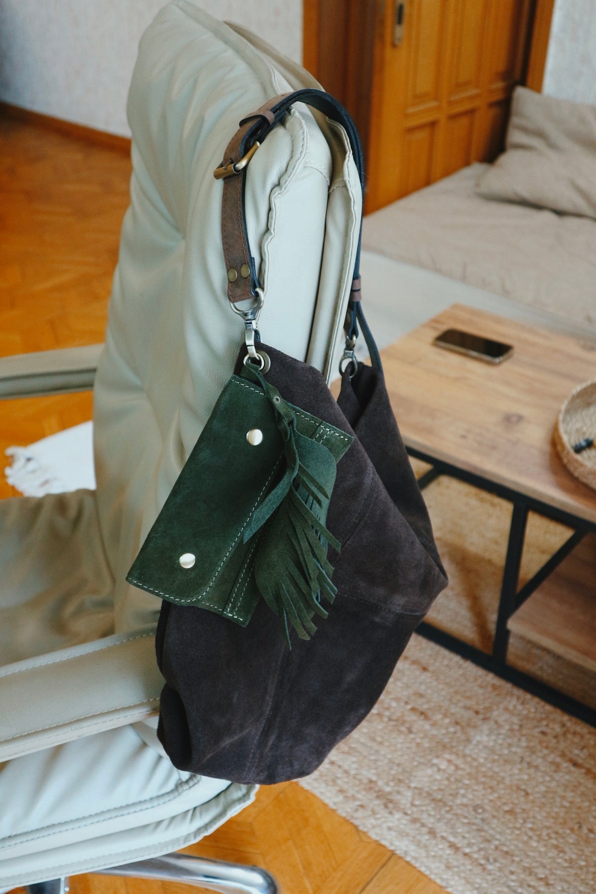 Black handbag with a green pouch attached, hanging on a chair in a room.