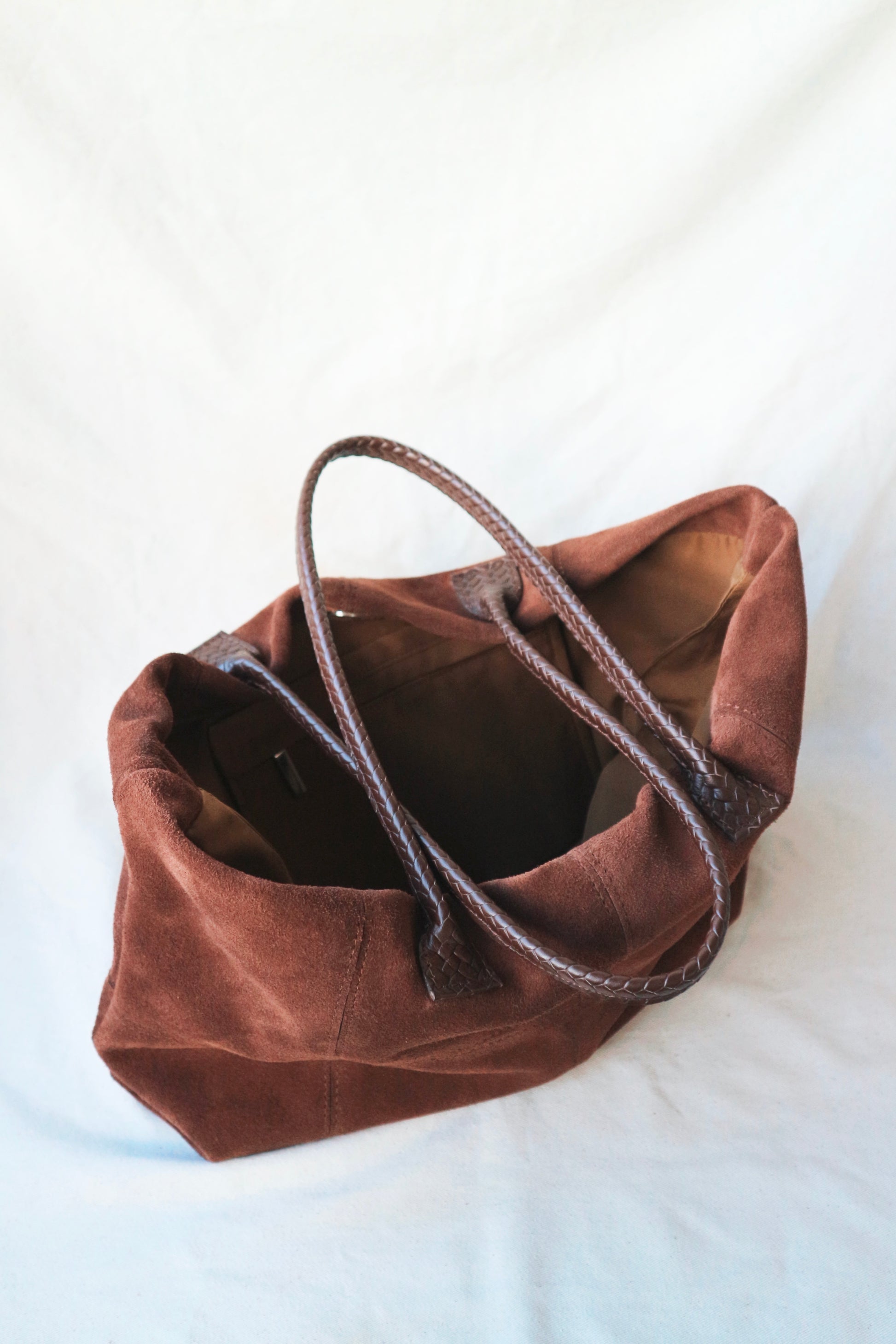 Brown suede handbag with leather handle on a white background