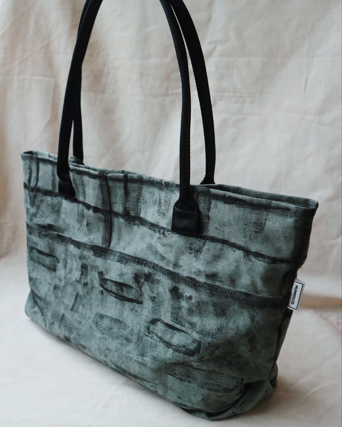 Green textured tote bag with black handles on a light background