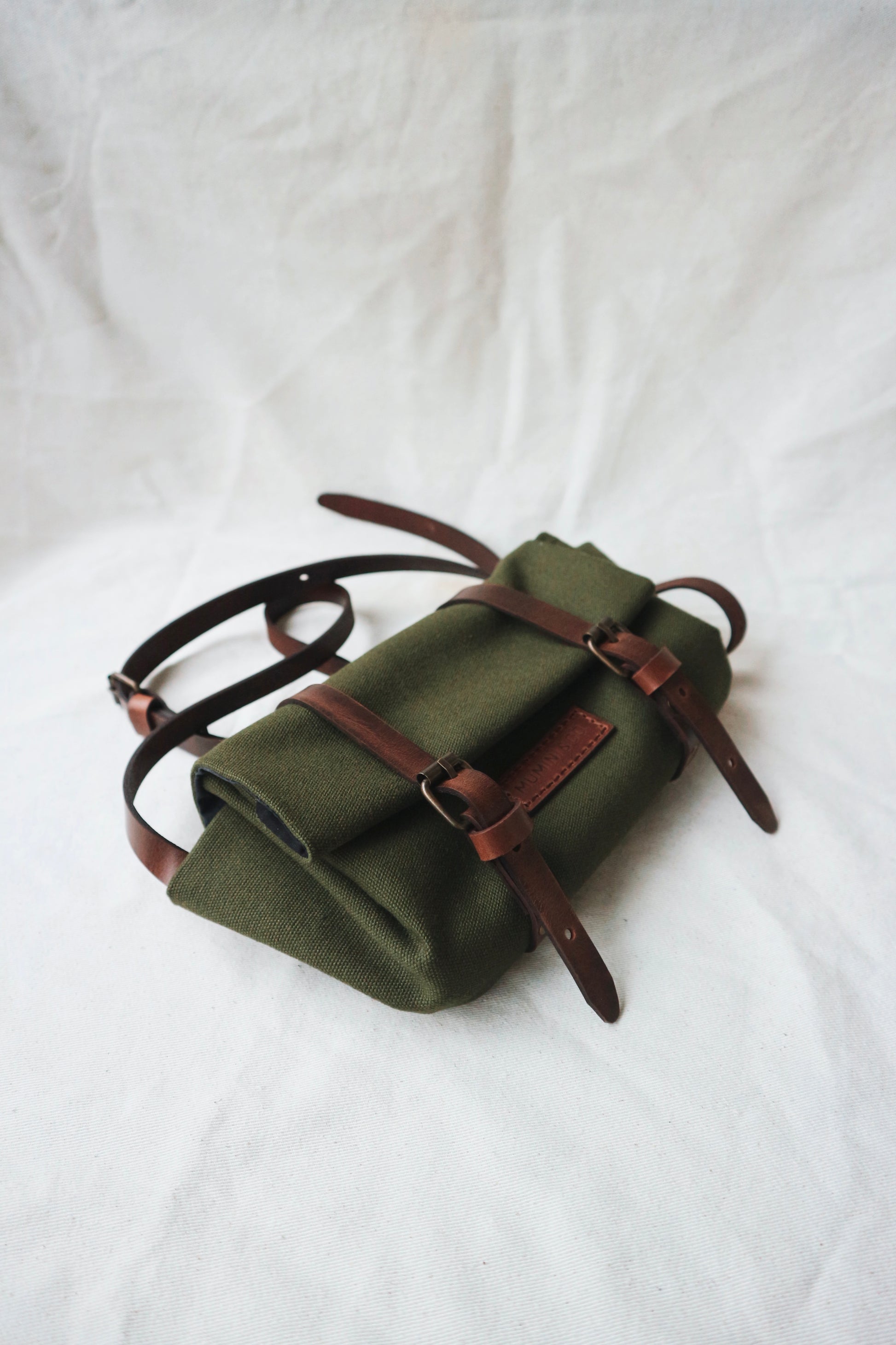 Green roll-up bag with brown straps on a white background